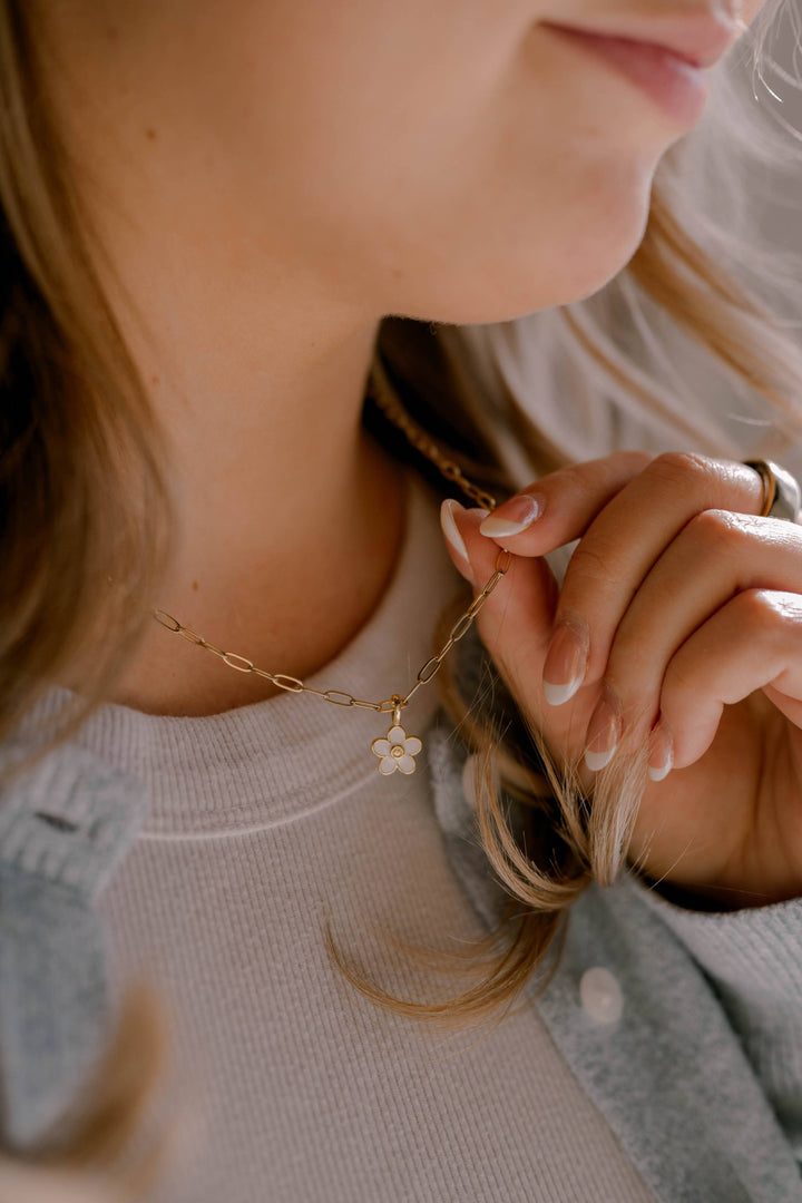 Close-up of a person wearing a delicate gold necklace with a flower pendant.