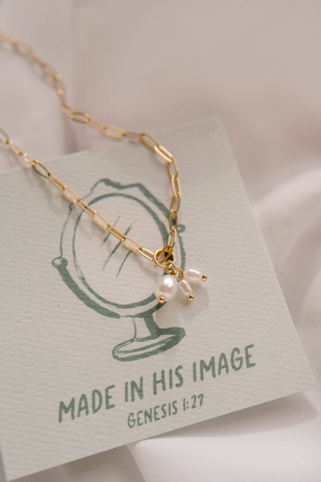 Gold necklace with a pendant on a card with 'Made in His Image' text