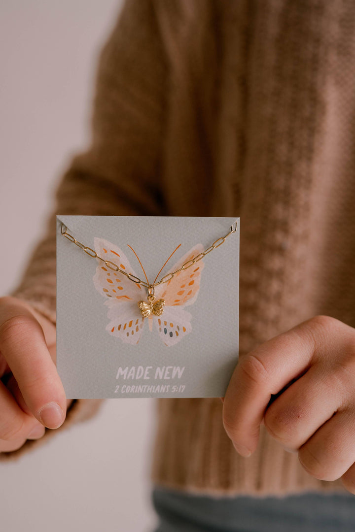Butterfly necklace on a card held by a person wearing a brown sweater.