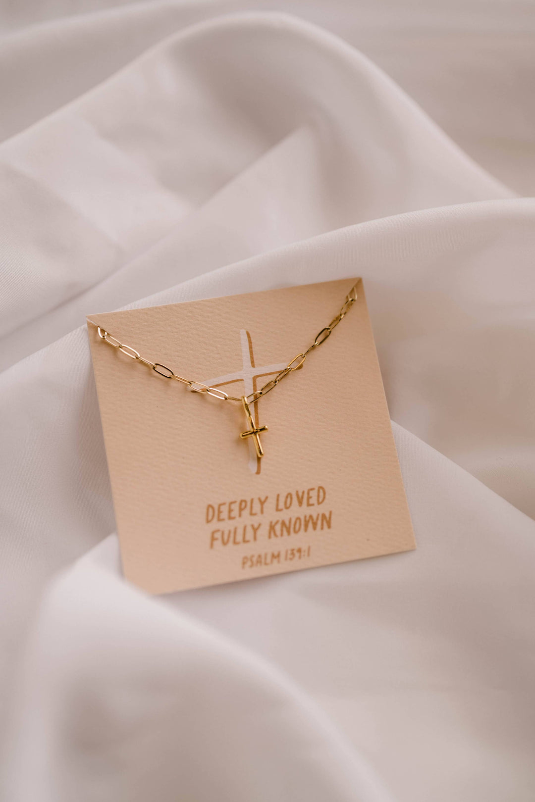 Gold necklace on a wooden card with text on a white fabric background