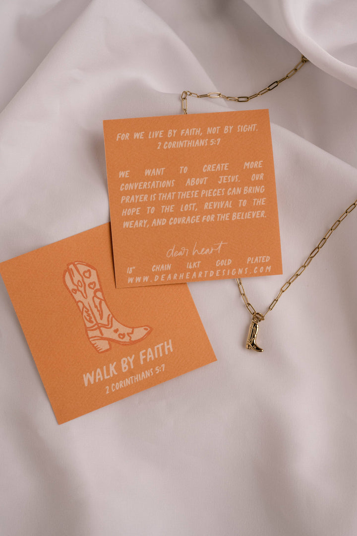 Necklace with a pendant on an orange card with text and a boot illustration, all on a light fabric background.