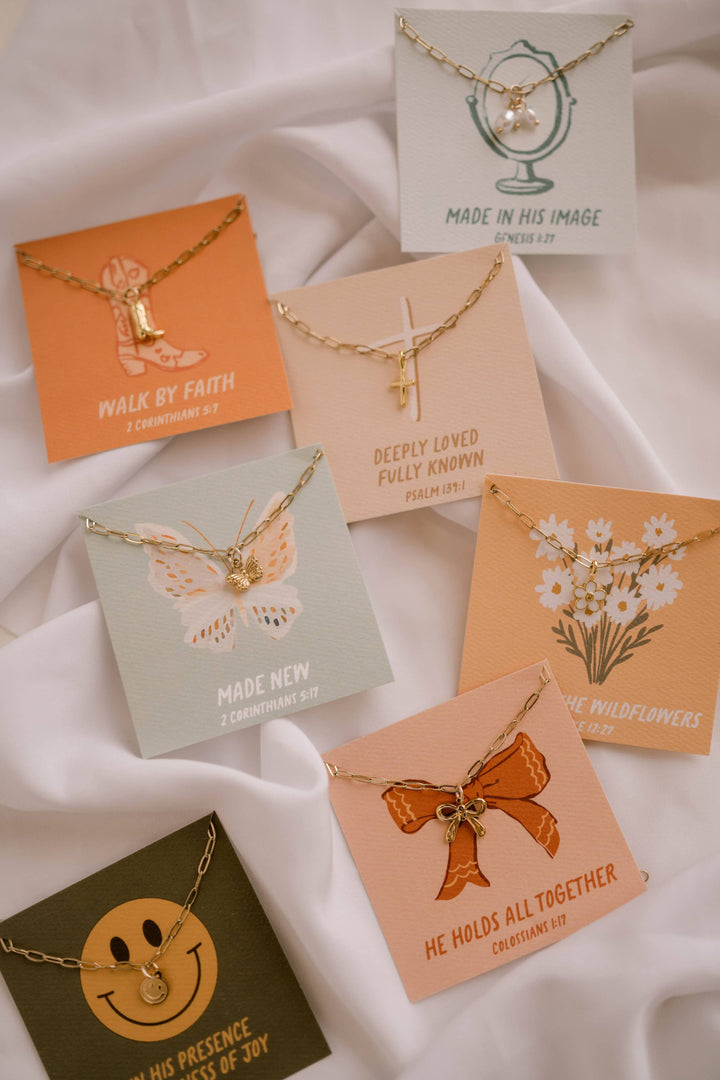 Collection of necklaces on cards with various designs and messages on a white fabric background.