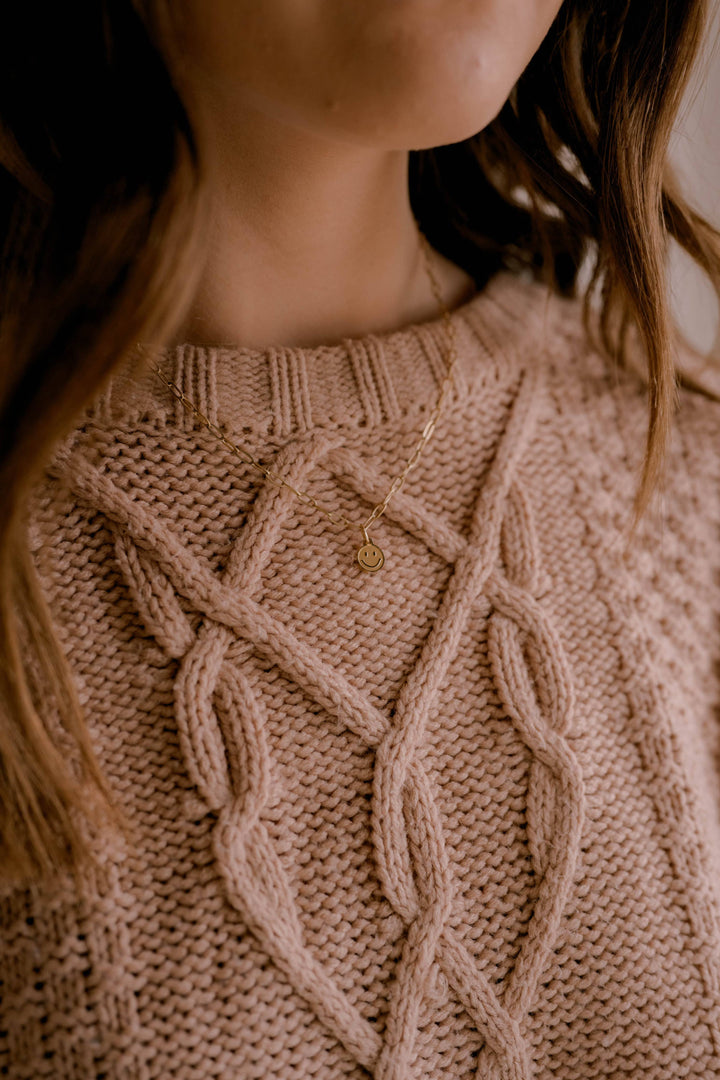 Close-up of a person wearing a beige knitted sweater with a subtle pattern.
