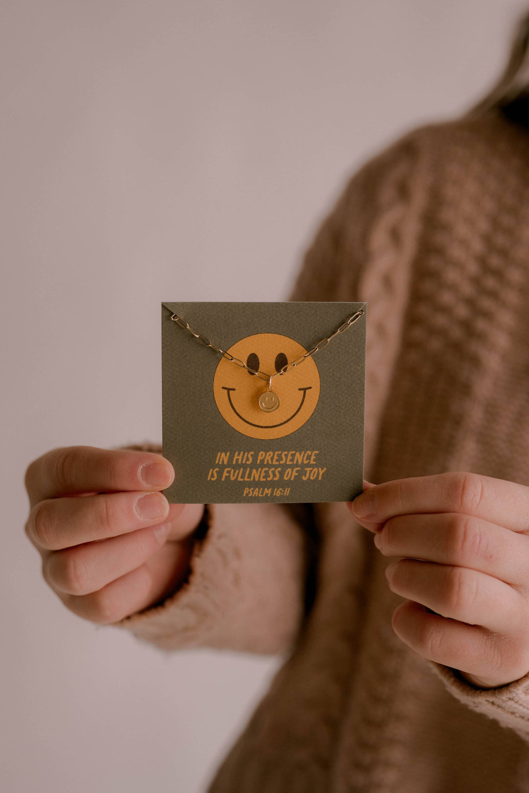 Person holding a necklace with a smiley face pendant and its packaging.