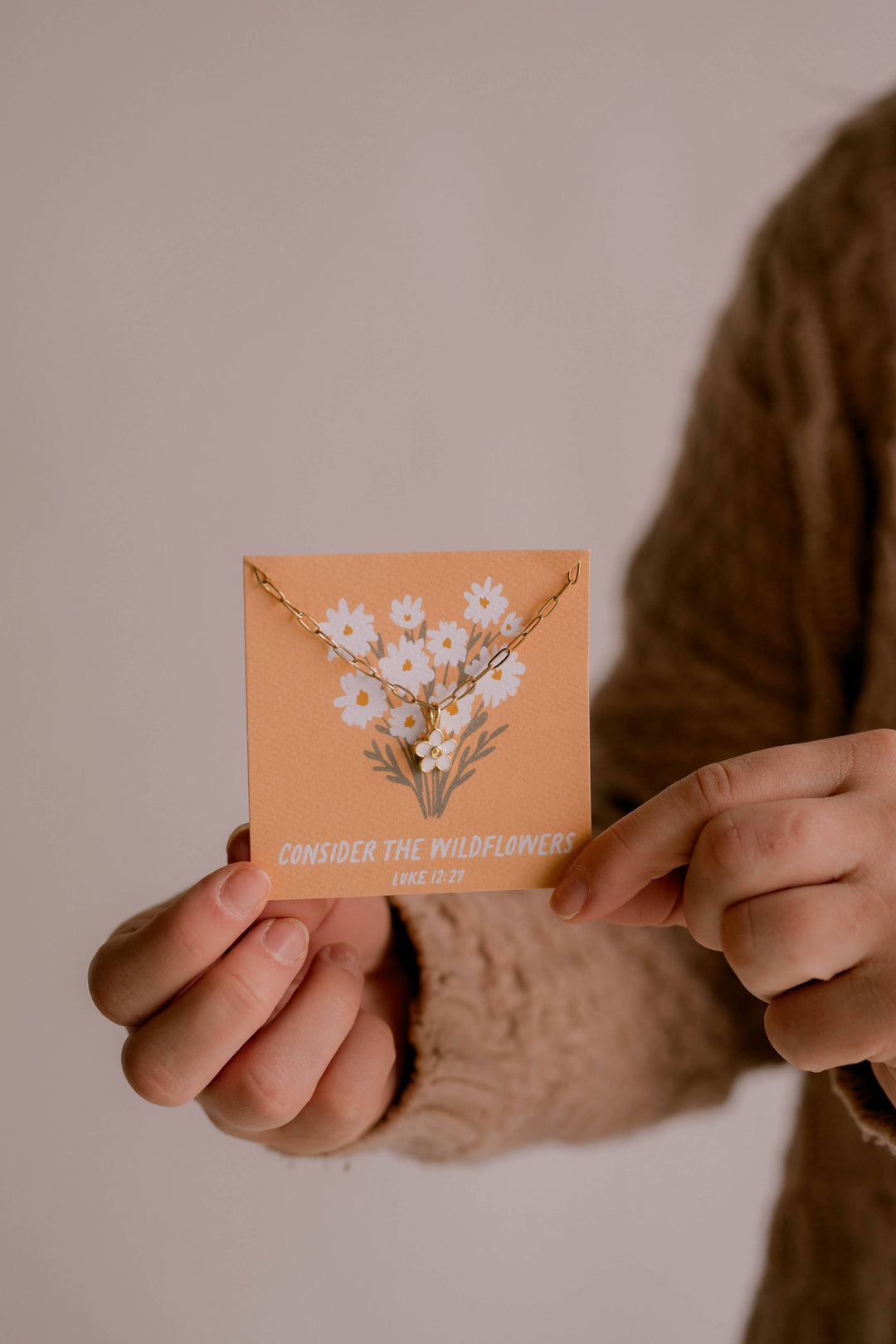 Person holding a small brown envelope with floral design against a neutral background