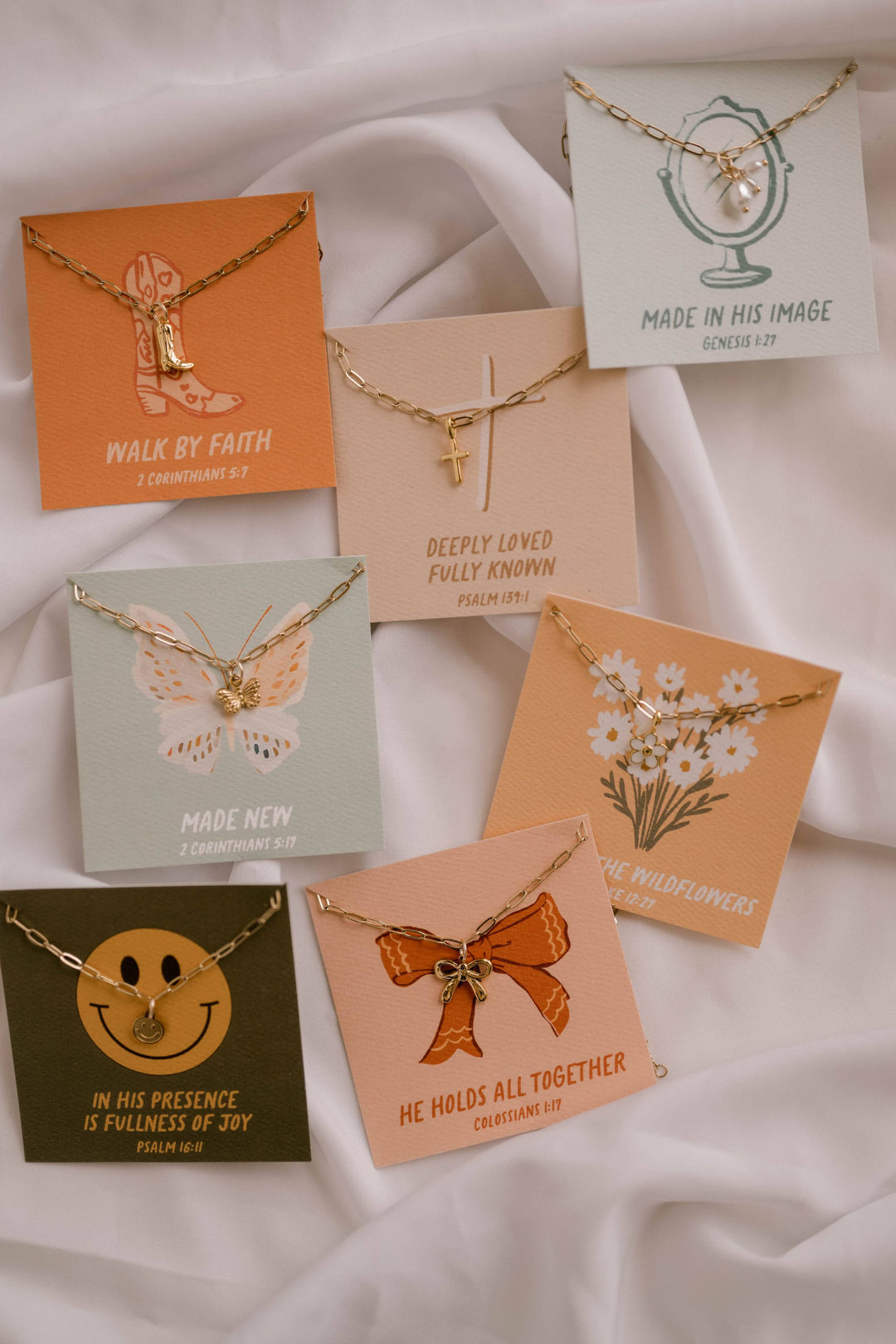 Collection of necklaces in various packaging with motivational phrases on a white fabric background