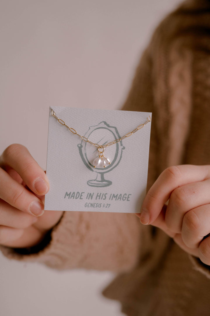Person holding a card with a necklace design and 'Made in His Image' text.