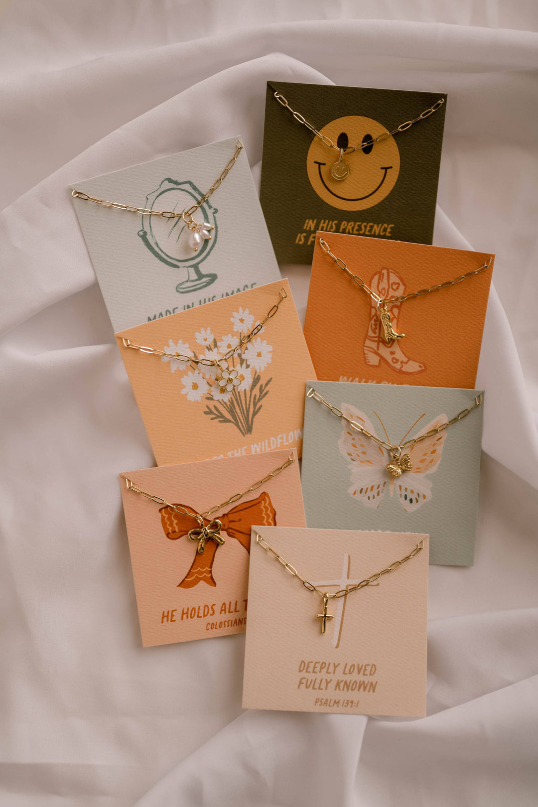 Collection of necklaces on display with matching card holders on a white fabric background