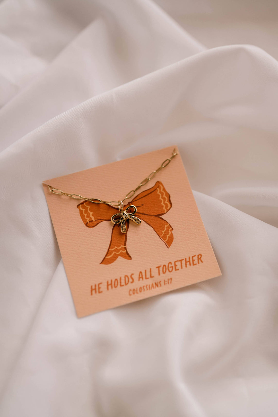 Necklace with a bow pendant on a matching card against a beige fabric background