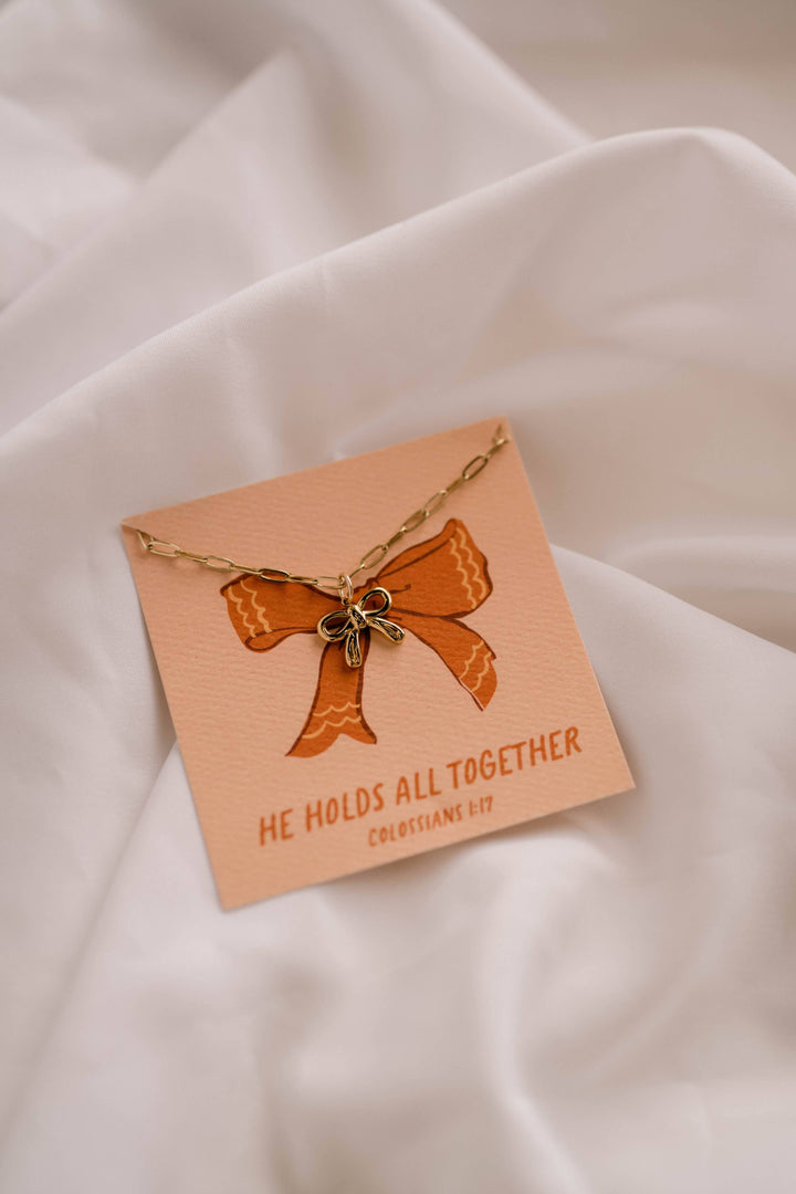 Necklace with a bow pendant on a matching card against a beige fabric background