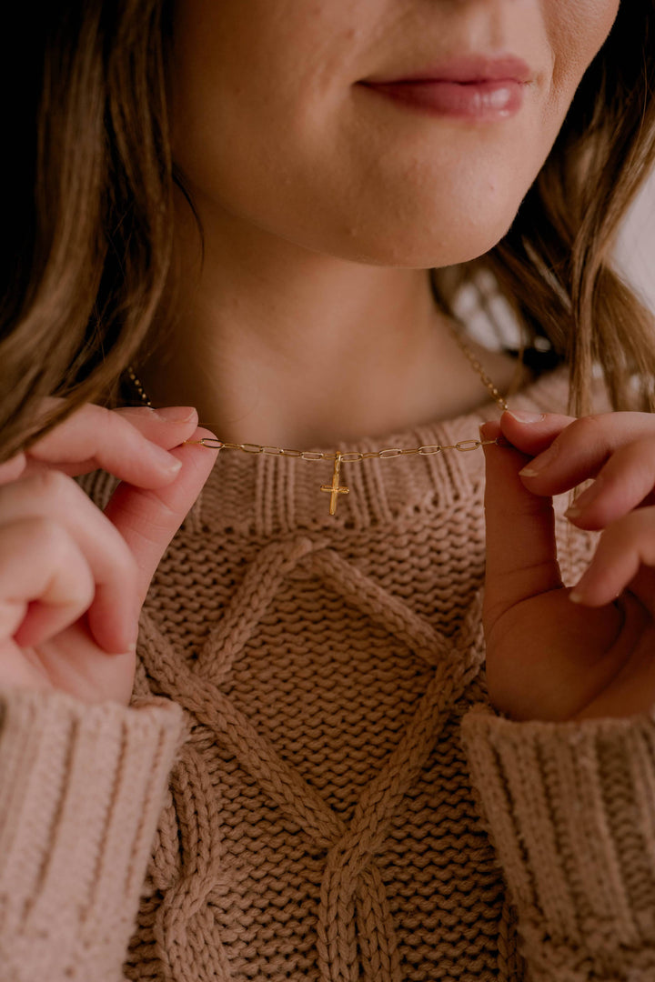 Close-up of a person wearing a brown knitted sweater with a necklace.