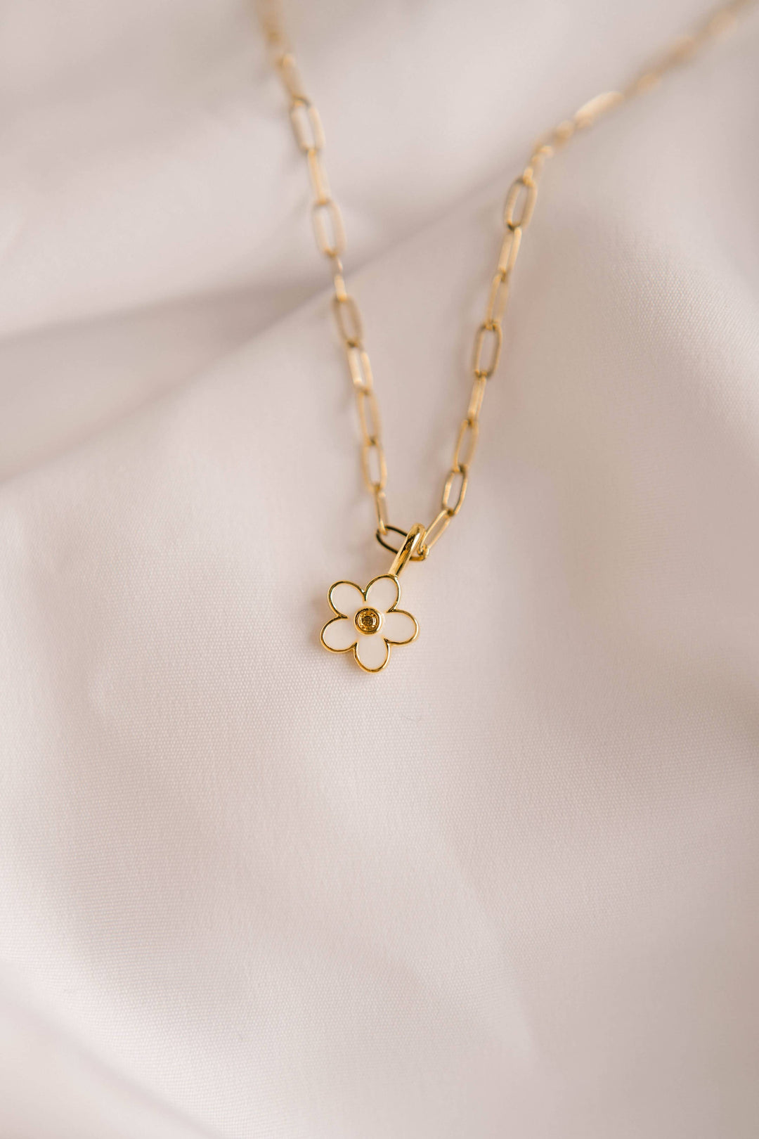 Gold necklace with a white flower pendant on a light background