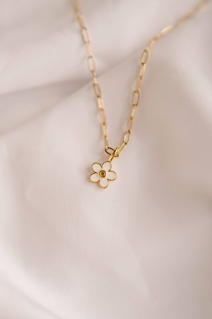 Gold necklace with a white flower pendant on a light background