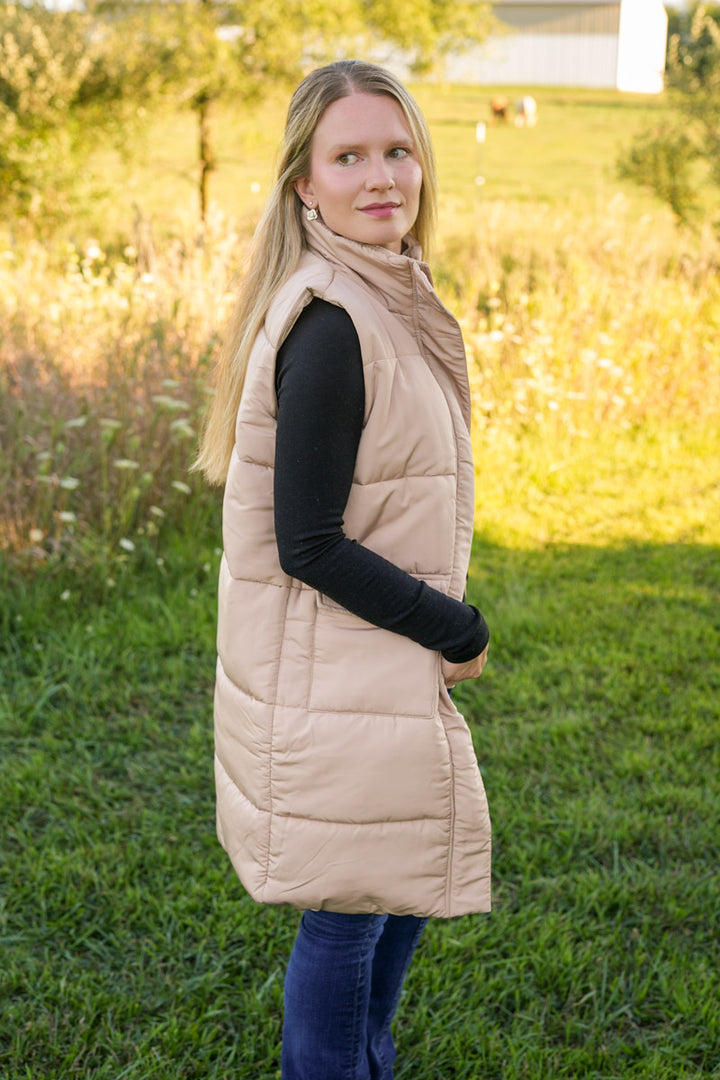 Woman wearing a long beige puffer vest in a grassy field