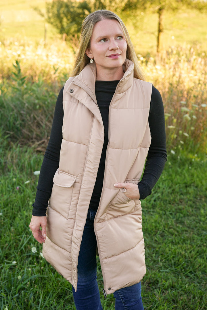 Woman wearing a long beige puffer vest in a field