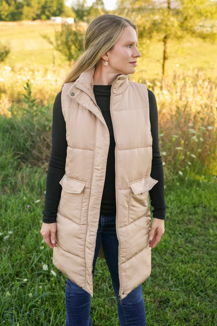Woman wearing a long beige puffer vest in a field