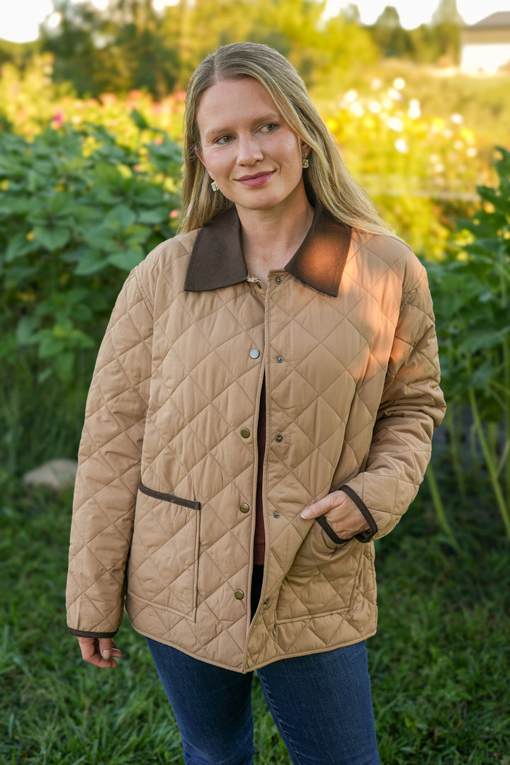 Woman wearing a tan quilted barn jacket with a brown collar in a field.