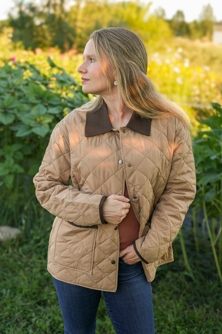Woman wearing a beige quilted jacket with a brown collar in an outdoor setting.