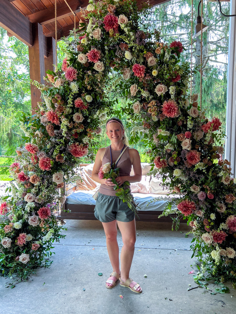 Emily Miller of Branch and Bloom Farms standing in front of a large floral arch on a porch.