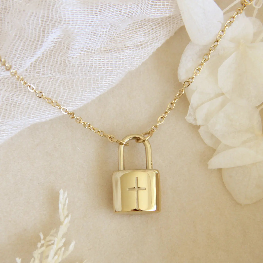 Gold padlock-shaped necklace with a cross on a beige surface