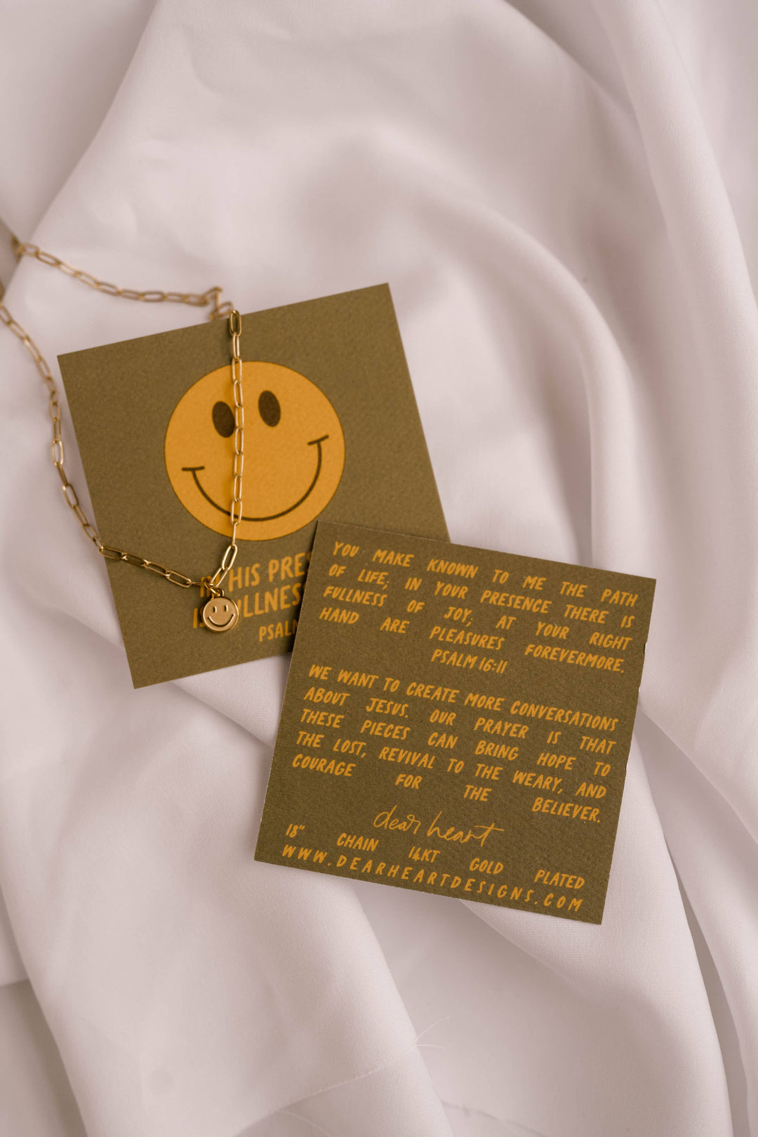 Smiley face necklace with a card on a white fabric background