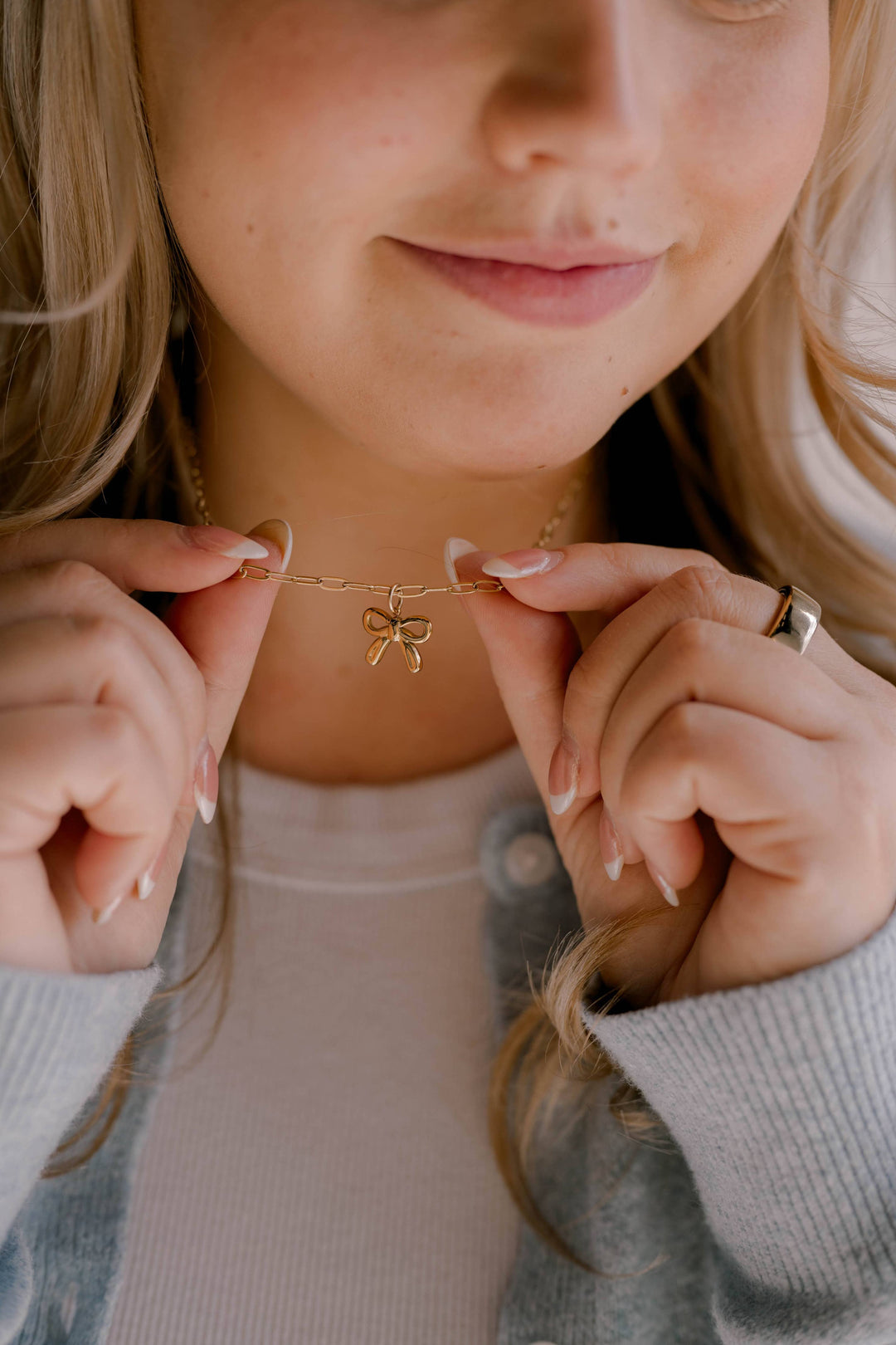 Close-up of a person holding a gold necklace with a bow pendant.