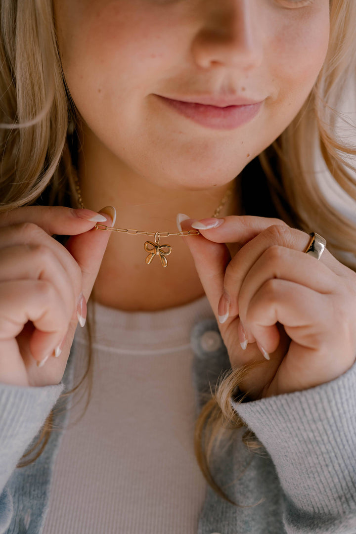 Close-up of a person holding a gold necklace with a bow pendant.