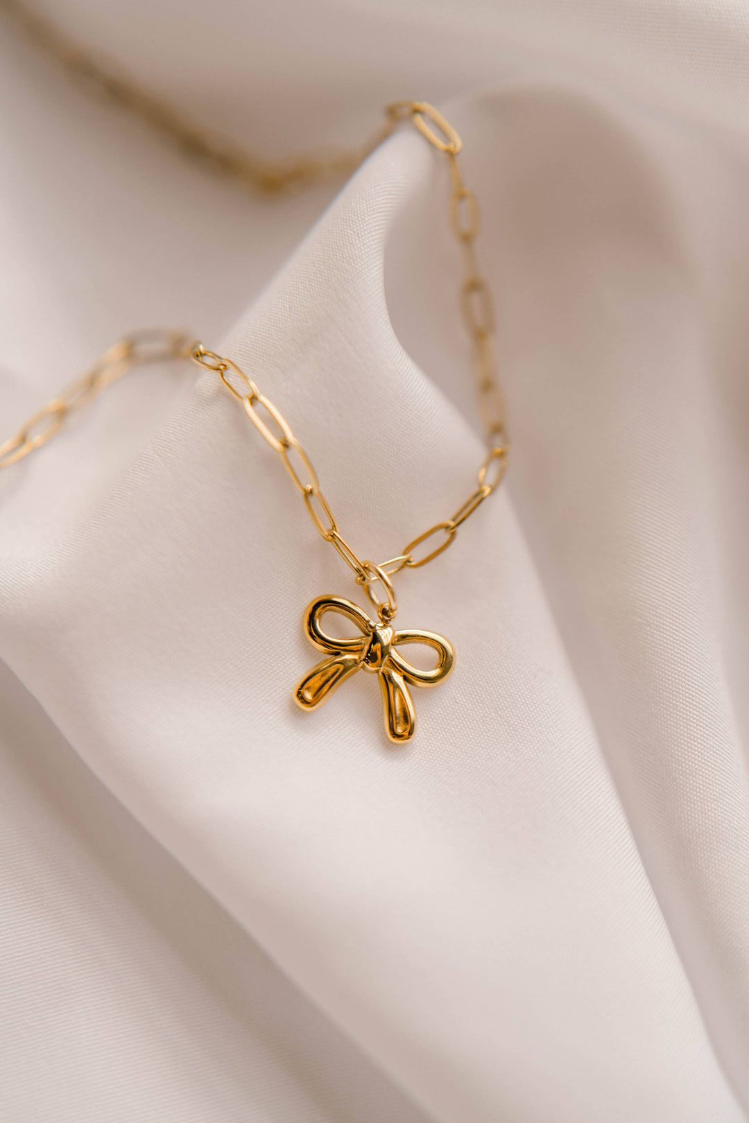 Gold necklace with a bow pendant on a soft beige fabric background