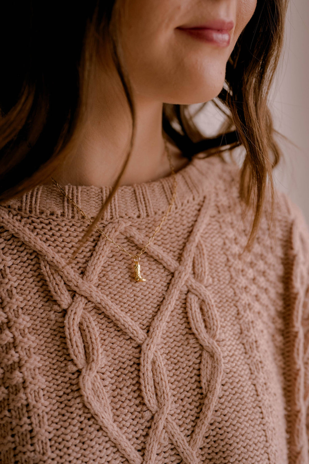 Close-up of a person wearing a cable knit sweater with a gold boot charm necklace.