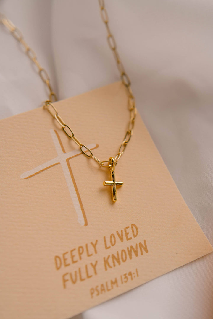 Gold necklace with a cross pendant on a beige card with text