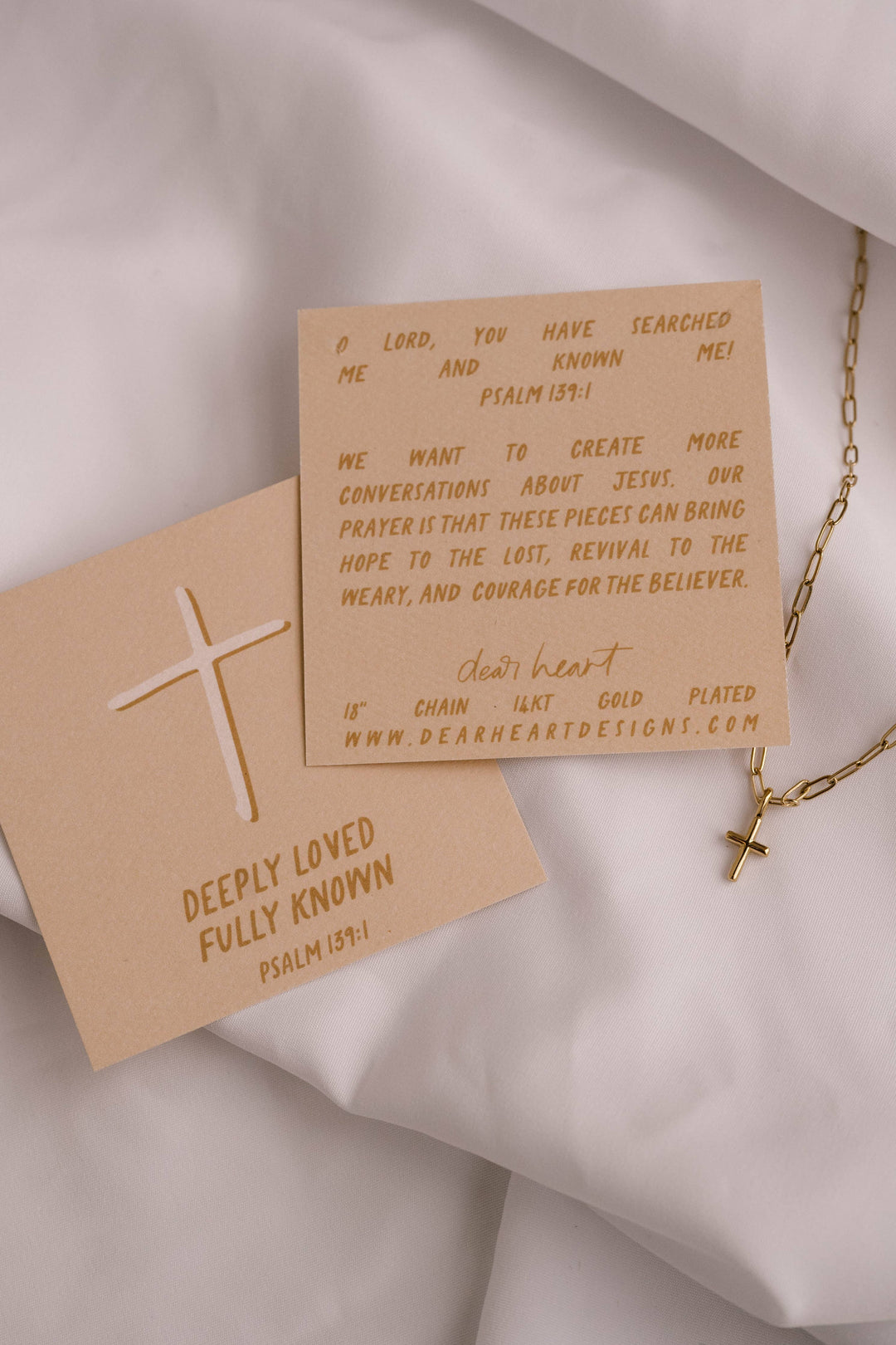 Two brown cards with text and a gold cross on a light fabric background