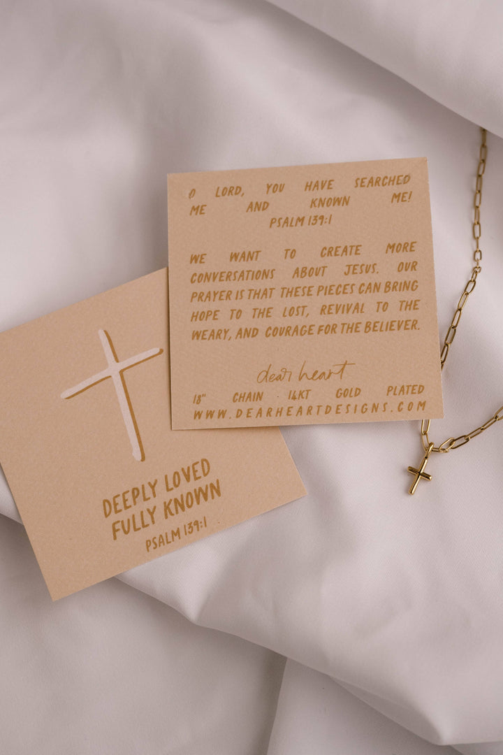 Two brown cards with text and a gold cross on a light fabric background