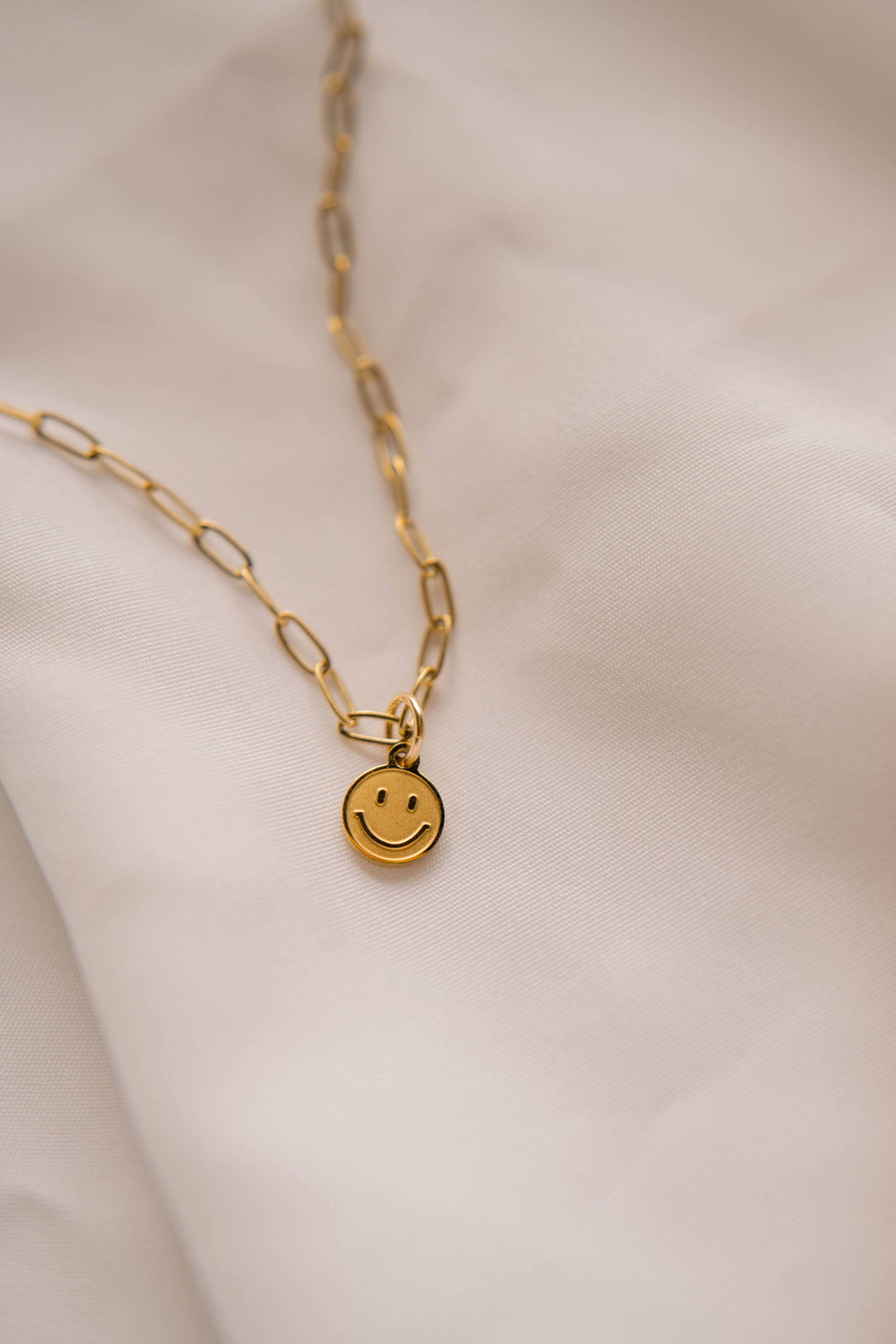 Gold necklace with a smiley face pendant on a soft beige background