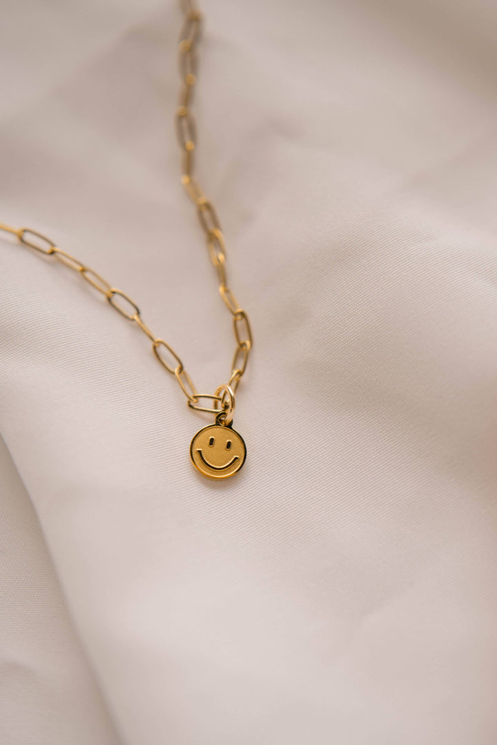 Gold necklace with a smiley face pendant on a soft beige background