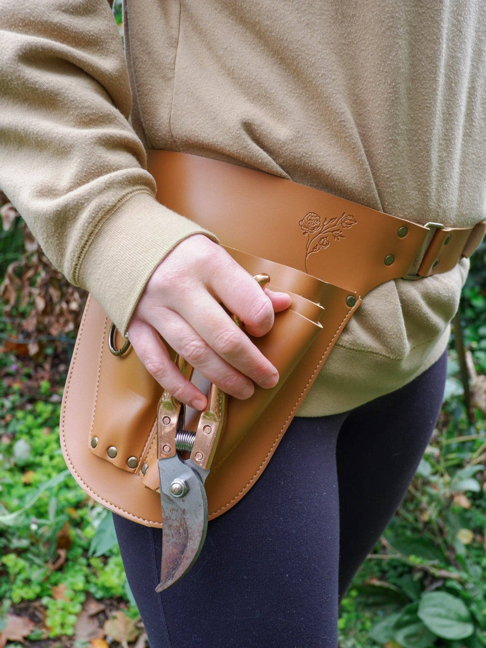 Person wearing a vegan leather gardening tool belt with pruning shears against a natural background
