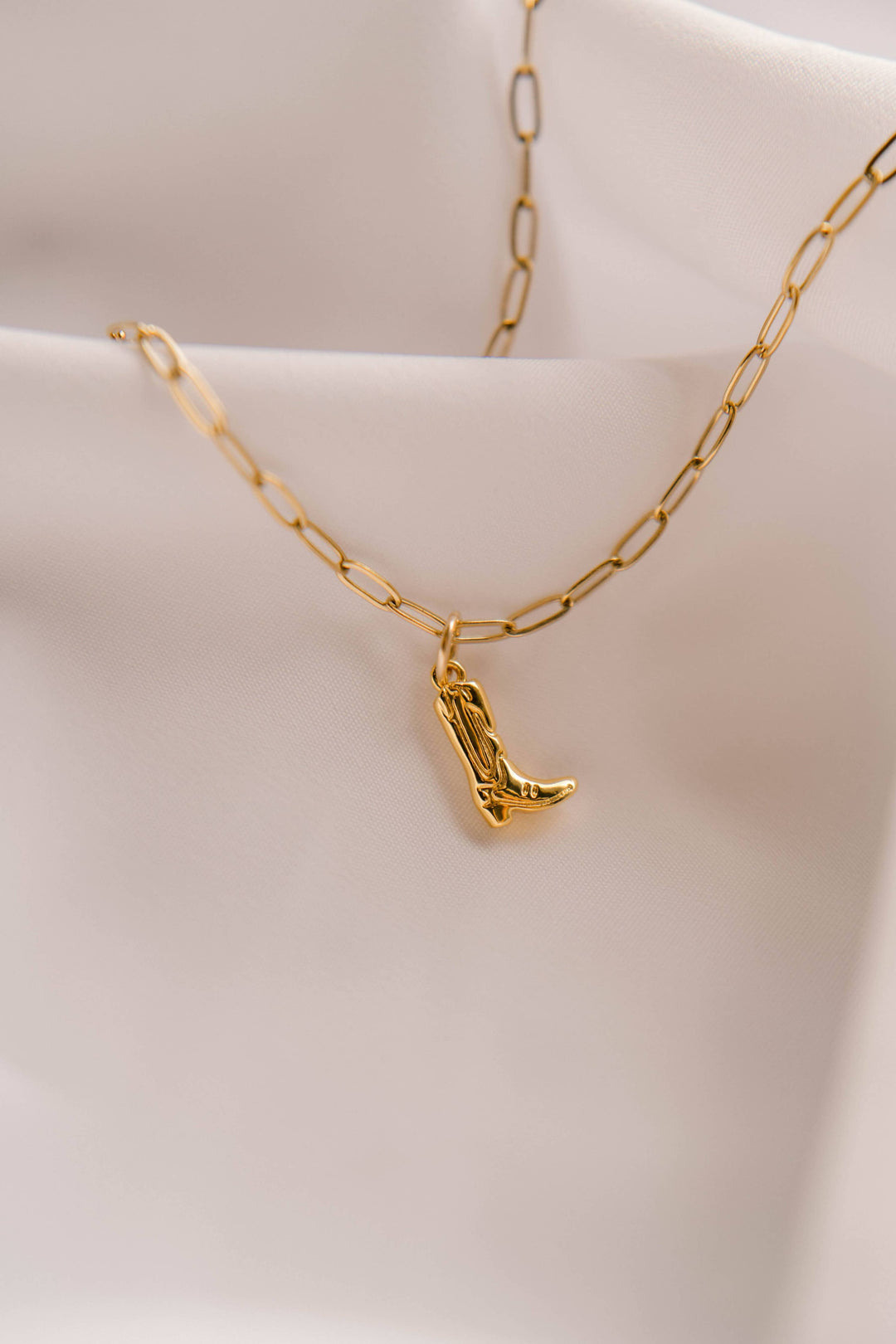 Gold necklace with a cowboy boot pendant on a light pink background