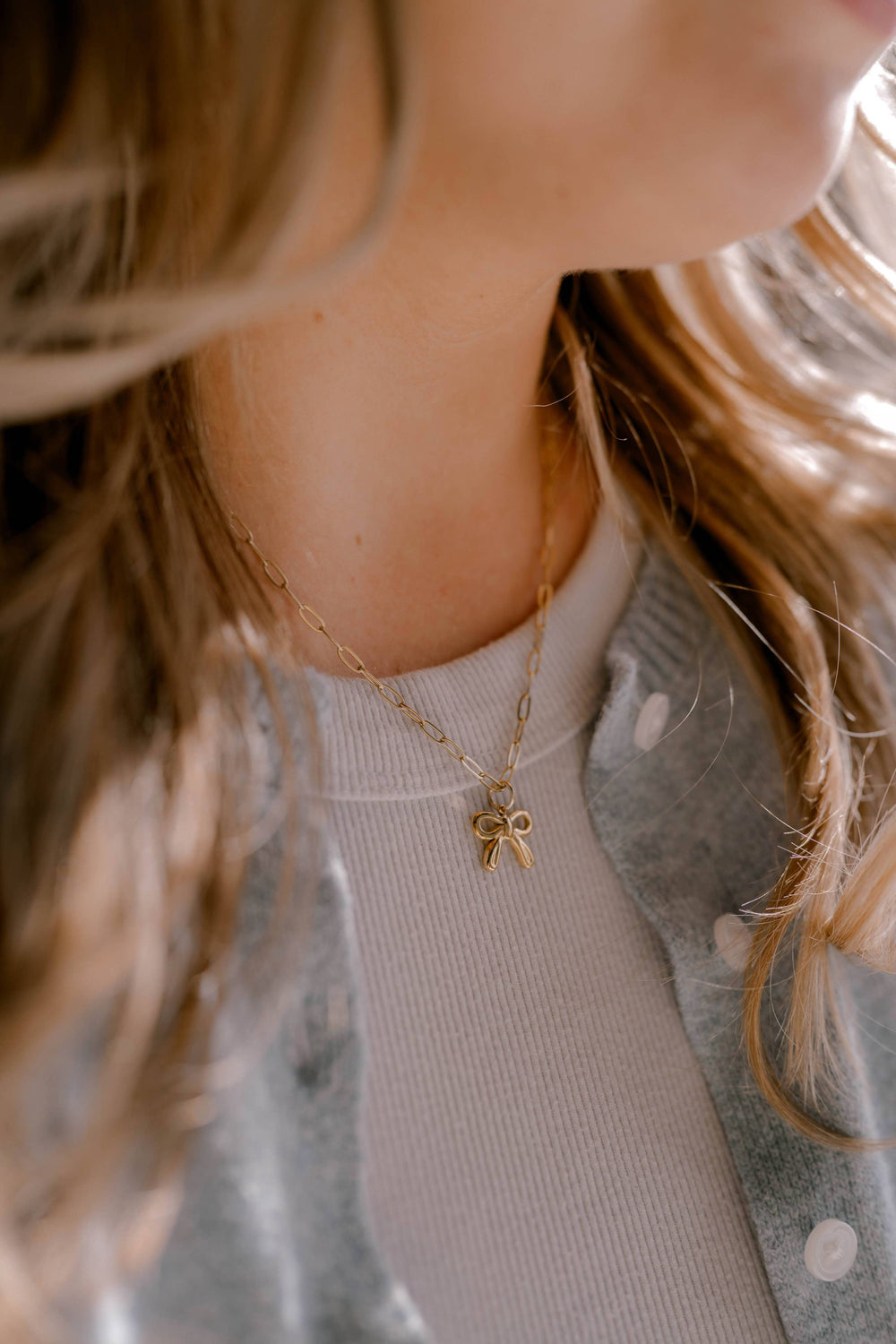 Close-up of a person wearing a gold necklace with a bow pendant.