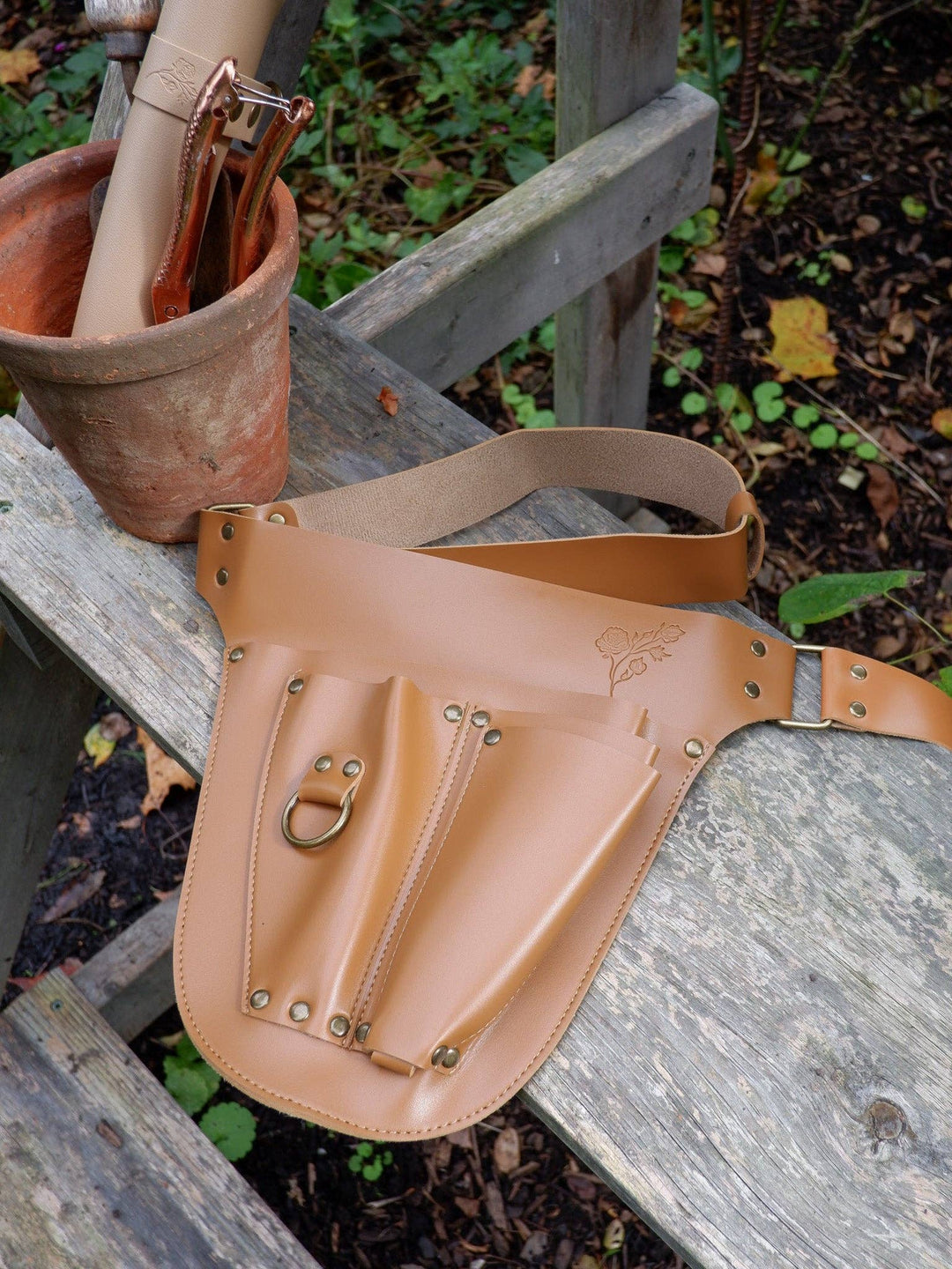 Brown vegan leather gardening toolbelt on a wooden bench with a plant pot in the background
