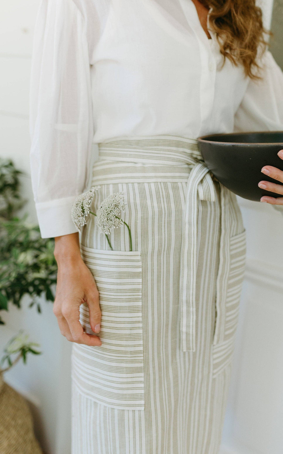 Person wearing a white shirt and striped green half garden apron holding a black bowl.