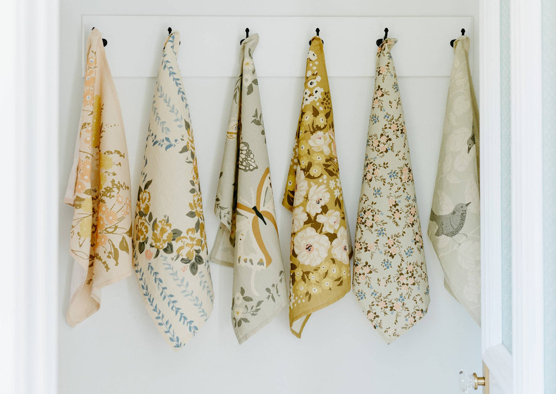 Set of floral and patterned tea towels hanging on a rack against a white wall.