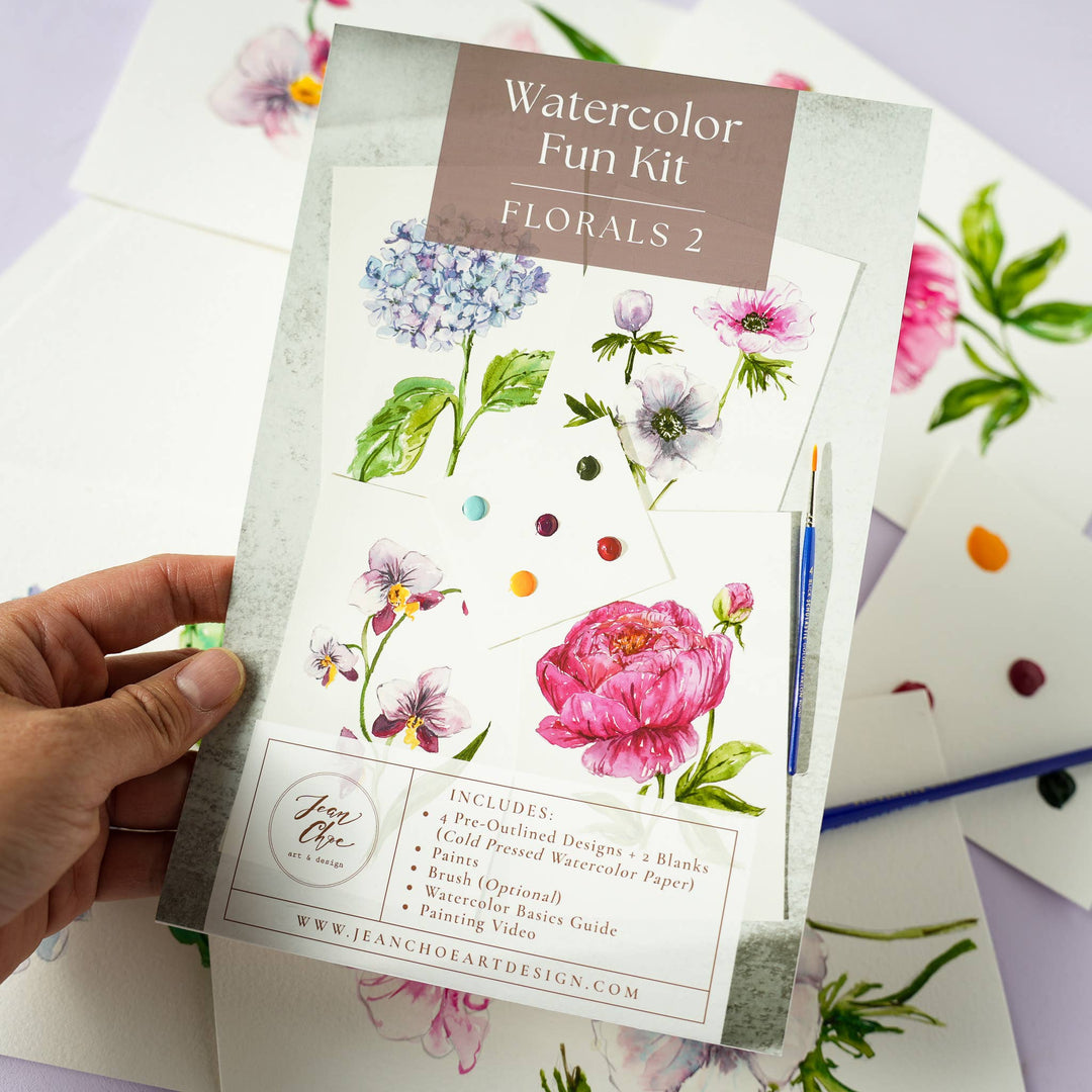 Watercolor Fun Kit with floral designs held by a hand on a light purple background.