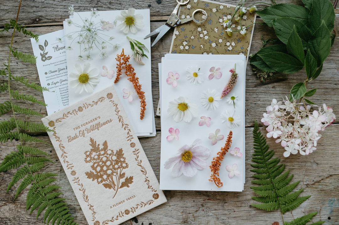 Pressed flowers and botanical cards on a wooden surface with greenery.