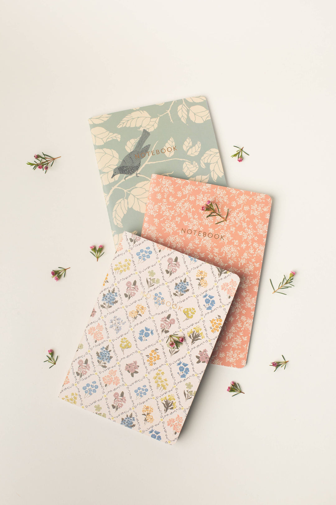 Three notebooks with floral and nature-themed designs on a light beige background.