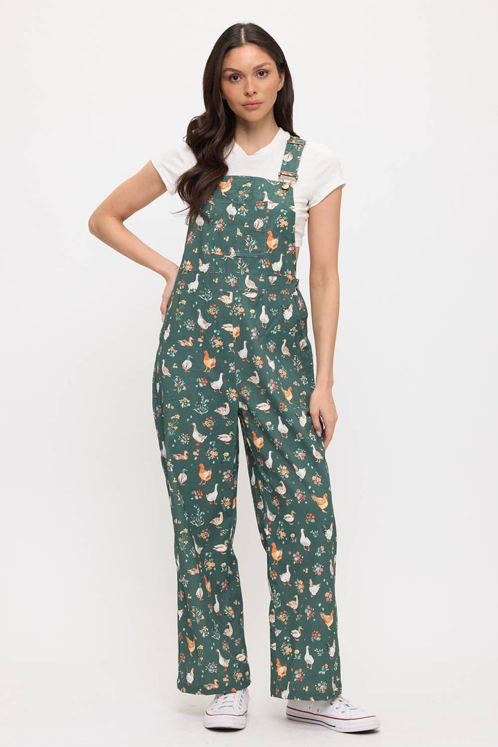 Woman wearing dark green overalls patterned with ducks, chickens and flowers on a white background