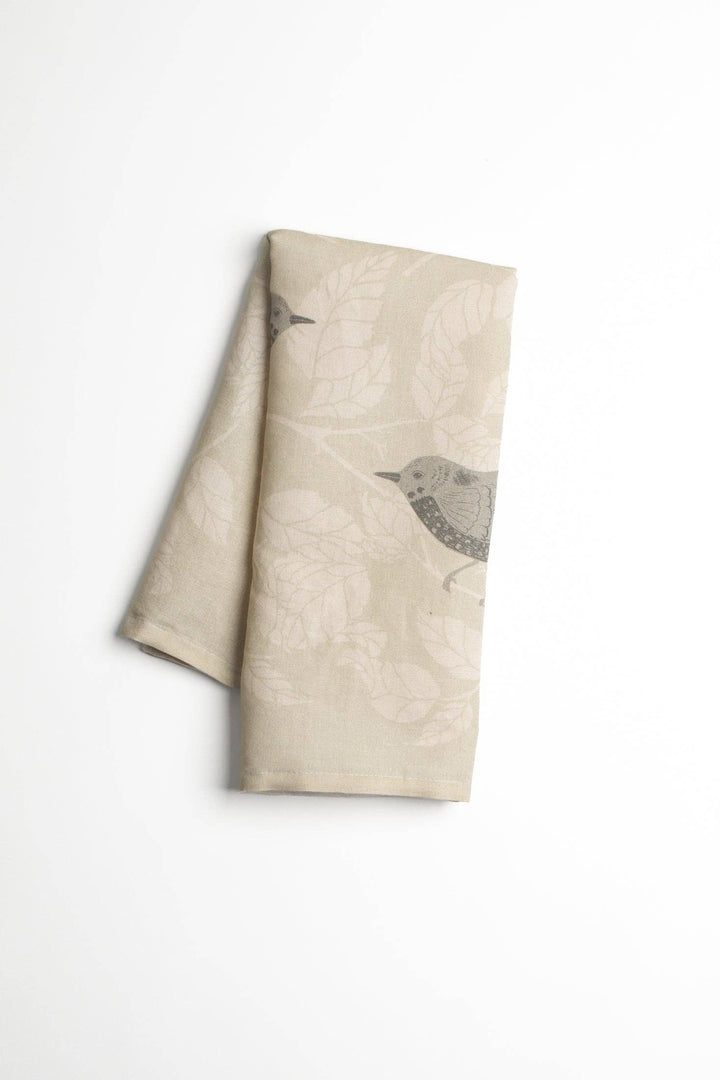 Folded beige linen tea towel with bird illustrations on a white background