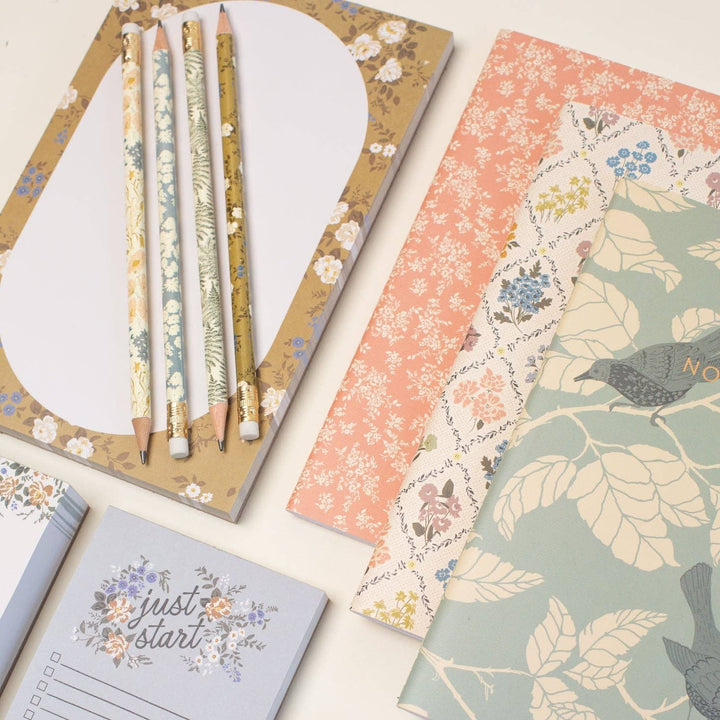 Set of notebooks and pencils with floral and nature-themed designs on a light background