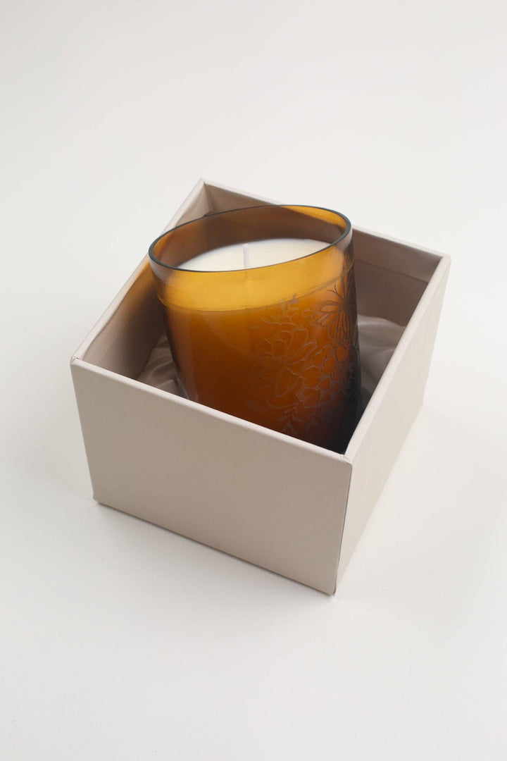 Candle in a textured glass holder inside a white box on a light gray background