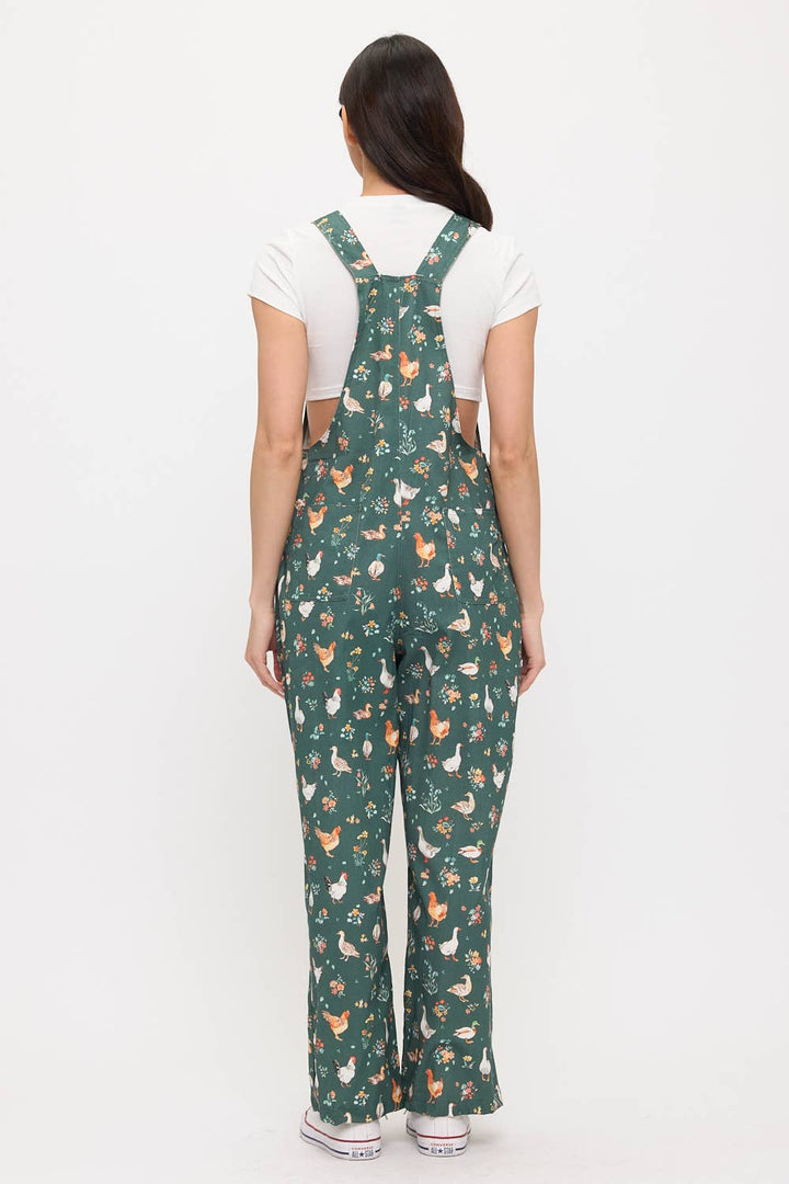 Woman wearing dark green ducks and chickens patterned overalls on a white background