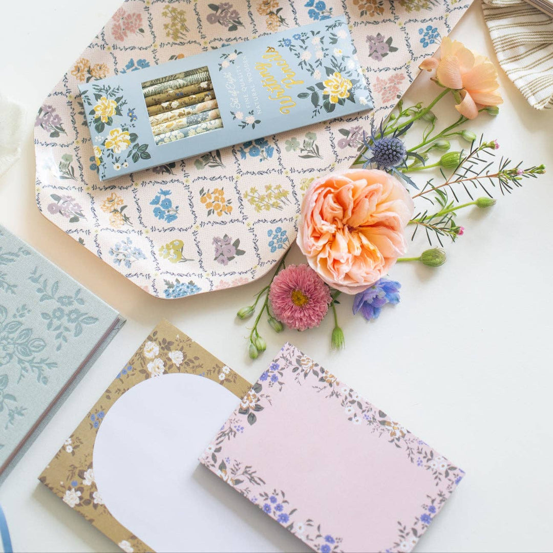 Floral stationery items including notebooks and a card on a patterned surface with flowers.
