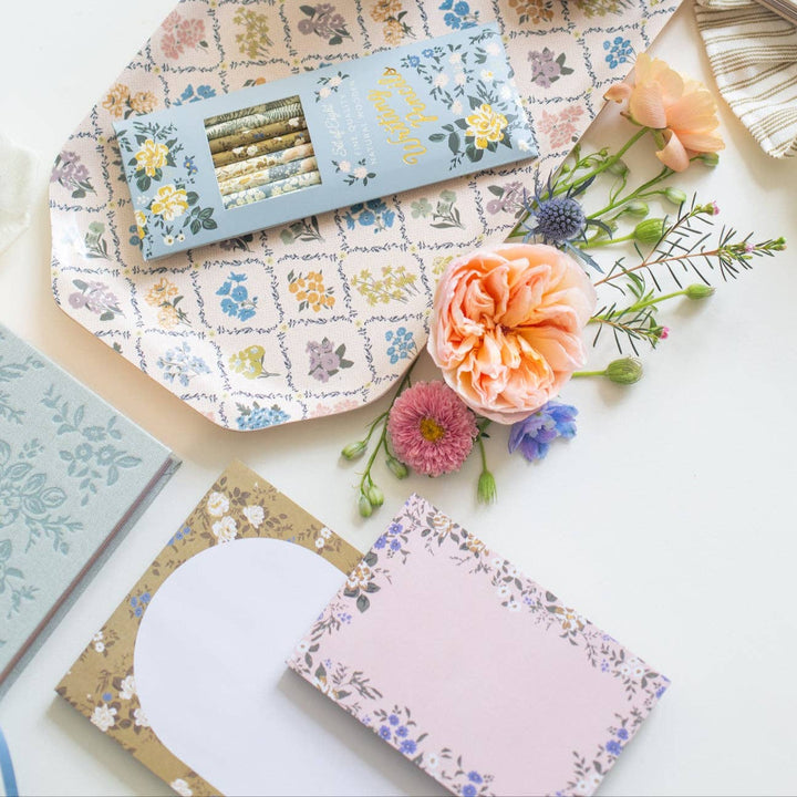 Floral stationery items including notebooks and a card on a patterned surface with flowers.